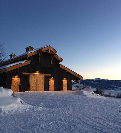 A black barn sits on top of a snow covered mountain.