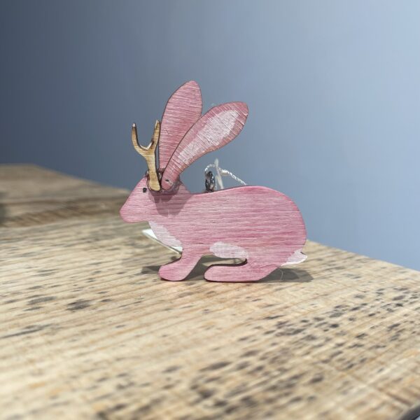 A pink jackalope ornament - 2022 sitting on top of a wooden table.