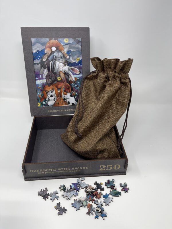 A box with the 250 PIECE WOODEN PUZZLE - "Dreaming Wide Awake" and a bag.