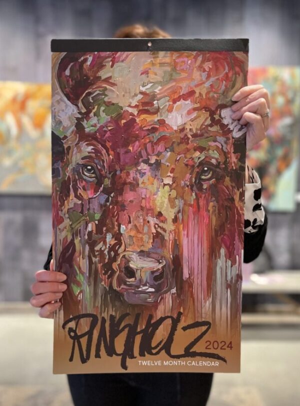 Person holding a colorful abstract painting of a bison with the text "Ringholz Calendar 2024" at the bottom.